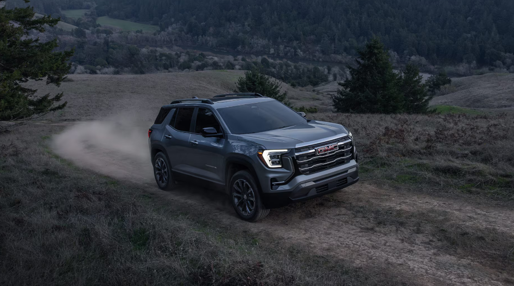 Gray GMC SUV driving on dirt road with trees in the background